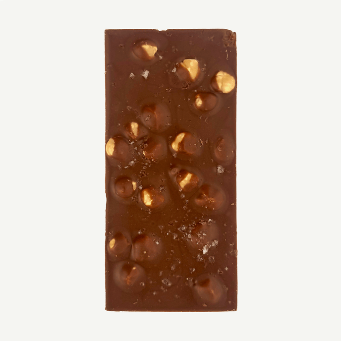 Milk chocolate block showing roasted hazelnuts, caramel crunch pieces and sea salt crystals