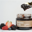A jar of Jumbleberry Jam with a piece of toast topped with jam, surrounded by fresh berries including blackberries, blueberries, and a strawberry.
