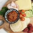 Platter of assorted cheeses, meats, and fruits with a bowl of condiment on a wooden board.
