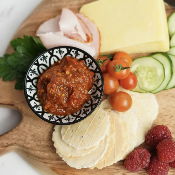 Platter of assorted cheeses, meats, and fruits with a bowl of condiment on a wooden board.