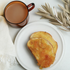 A jar of breakfast marmalade on a white plate with a piece of toast, alongside a cup of tea and a decorative branch in the background.