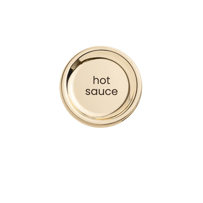 A gold metal lid for a hot sauce bottle with the text 'hot sauce' lasered on it.