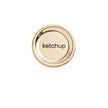 A brushed gold metal disc with the word 'ketchup' lasered in the center, designed as a lid for a condiment bottle.