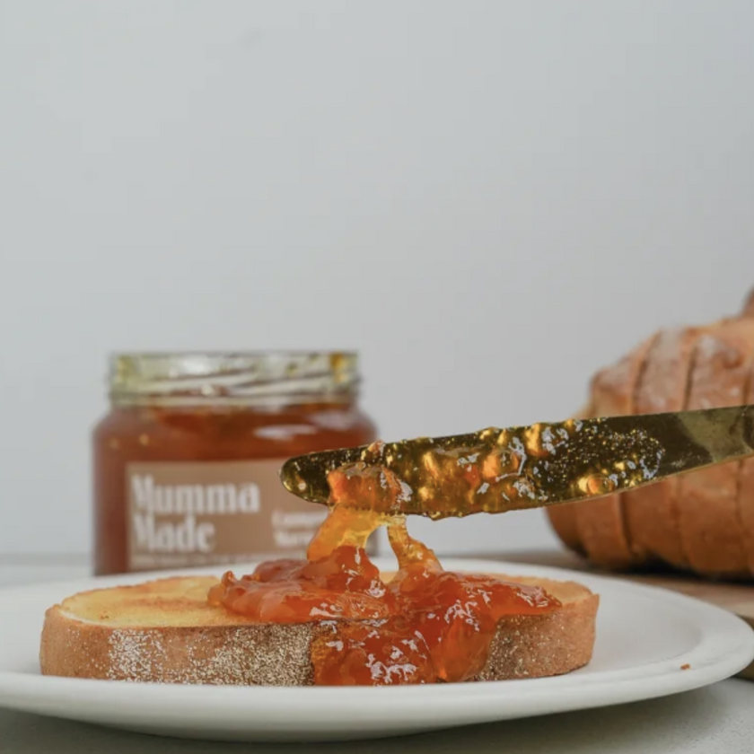 A jar of Seville orange and whisky marmalade with a slice of bread and butter in the foreground, covered in marmalade, and a knife resting on the plate.