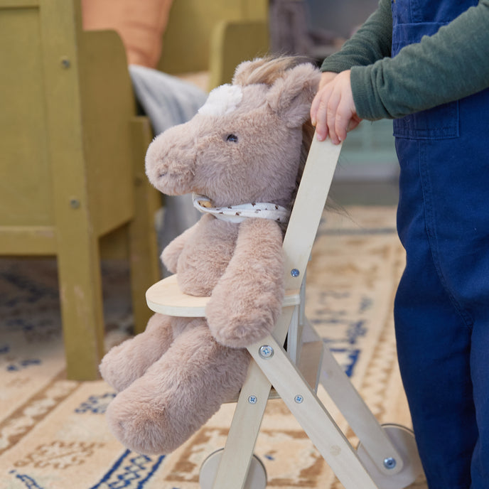 Child holding a plush toy horse on wheels in a room with furniture and a rug.