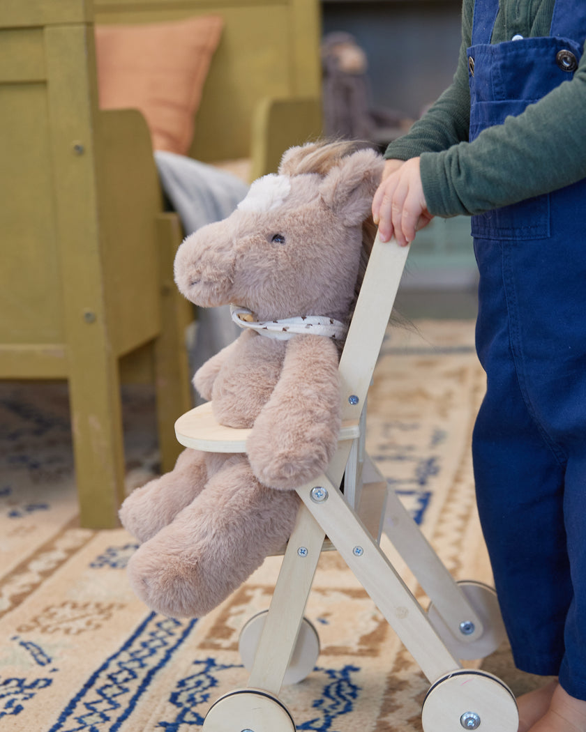 Child holding a plush toy horse on wheels in a room with furniture and a rug.