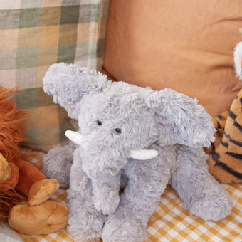 Plush elephant toy on a checkered blanket with colorful pillows in the background