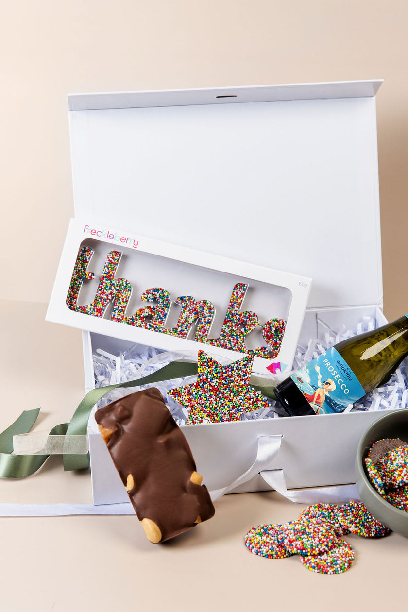 Gift box with wine, chocolate, and colorful lettered treats on a beige background