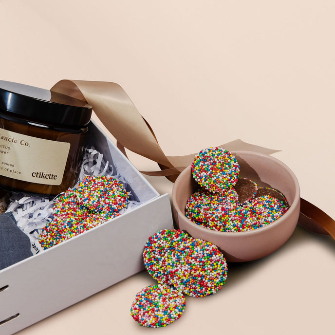 Colorful sprinkled candies in a pink bowl with a white box on a beige background