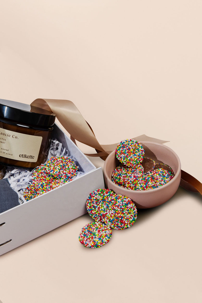 Colorful sprinkled candies in a pink bowl with a white box on a beige background