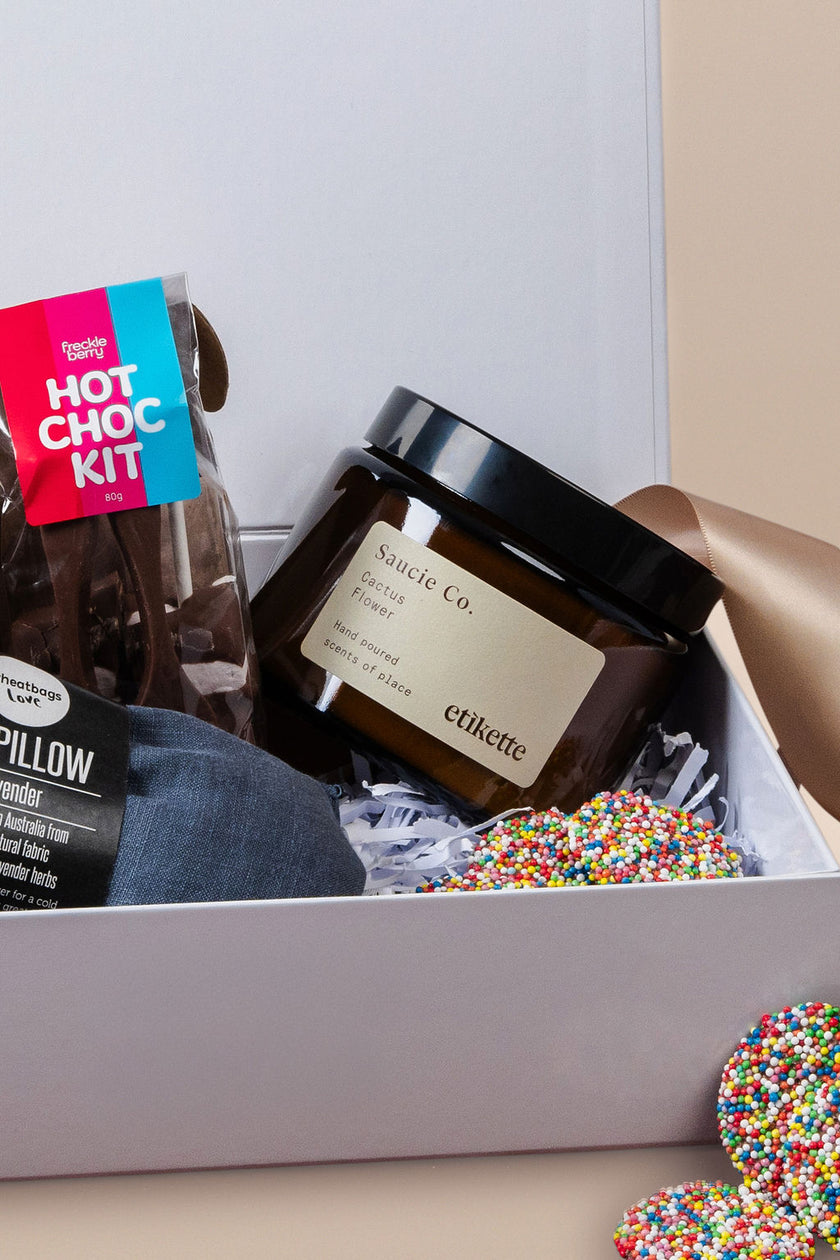 Gift box with a jar, pillow, and hot chocolate kit on a light background