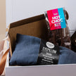Gift Box containing a blue eye pillow and a hot chocolate kit on a light background