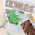 Decorative Christmas-themed gift box with a green tree and colorful letters on a beige background.