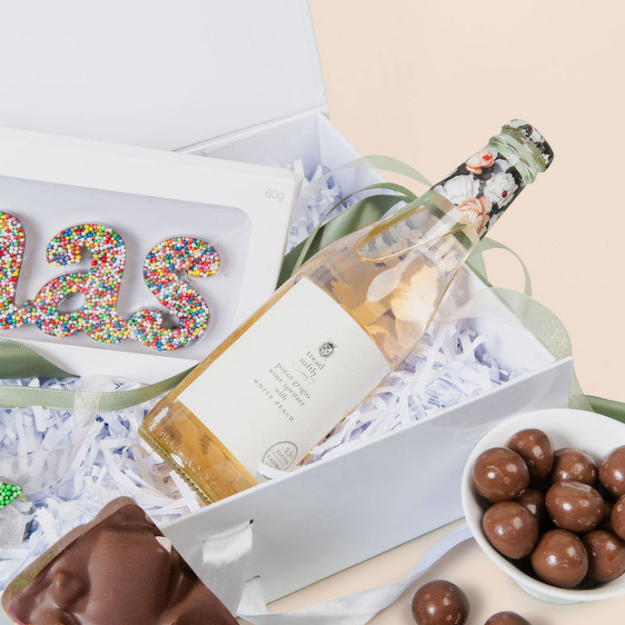 Gift box with a bottle of wine, cookies, and chocolates on a light background