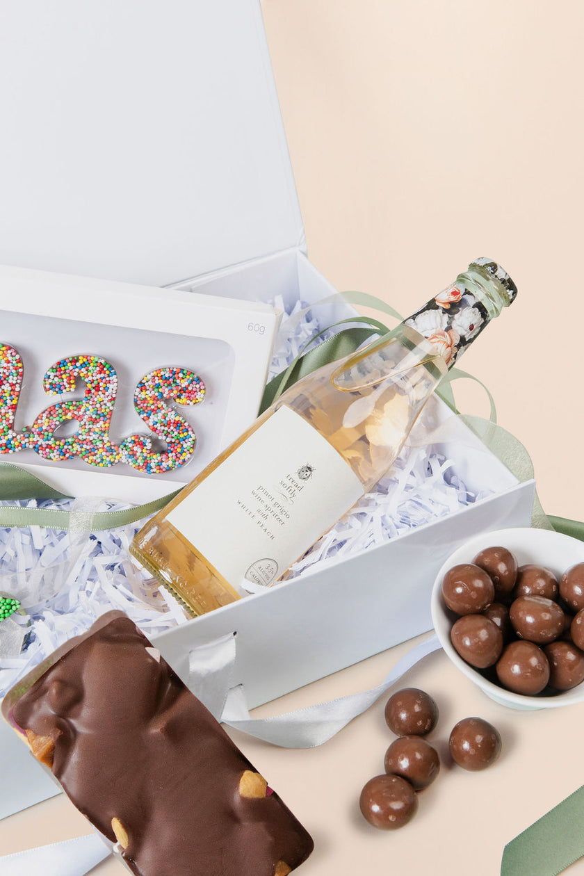 Gift box with a bottle of wine, cookies, and chocolates on a light background