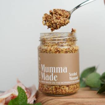 Jar of 'Mumma Made' seeded mustard with a spoonful above, on a wooden board.