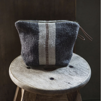 Textured pouch with striped pattern on a wooden stool against a dark background