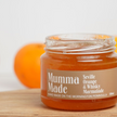 Jar of Mumma Made Seville Orange & Whisky Marmalade on a wooden surface with an orange in the background.