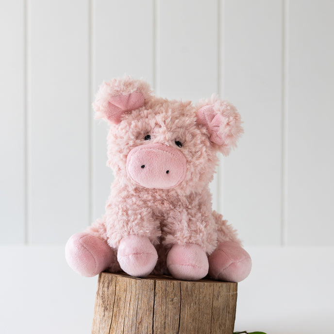 Pink plush pig toy on a wooden block with a white background