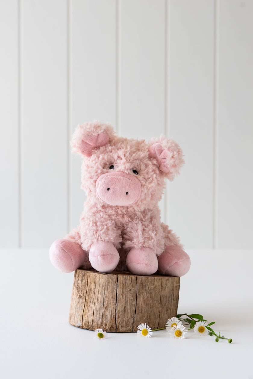 Pink plush pig toy on a wooden block with a white background