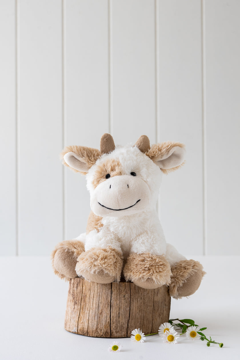 Plush cow toy on a wooden stump with a white background