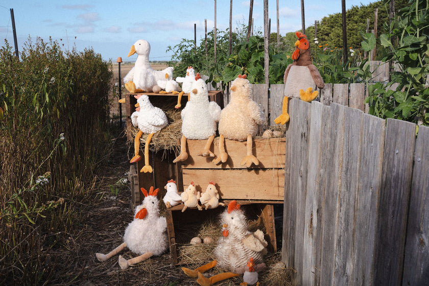 Plush toy chickens and ducks on a wooden structure in an outdoor setting.