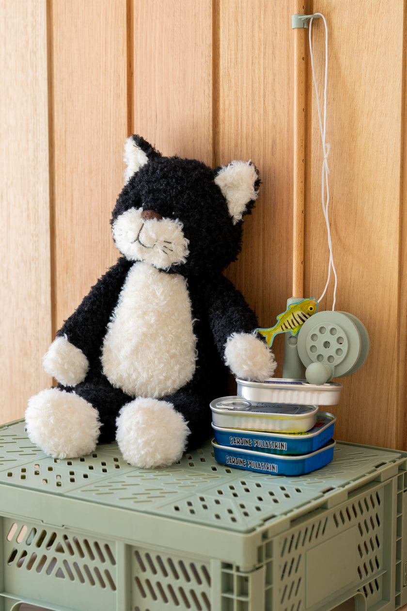 Black and white cat-shaped plush toy on a green crate with a wooden background