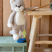 Plush cat toy with a string toy on a green crate next to a wooden stool.
