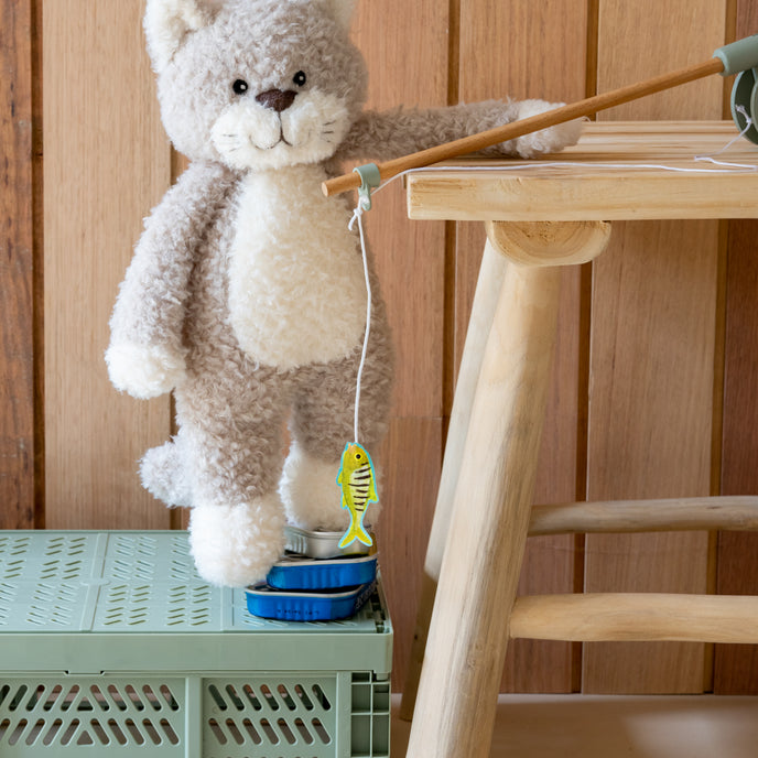 Plush cat toy with a string toy on a green crate next to a wooden stool.