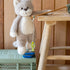 Plush cat toy with a string toy on a green crate next to a wooden stool.