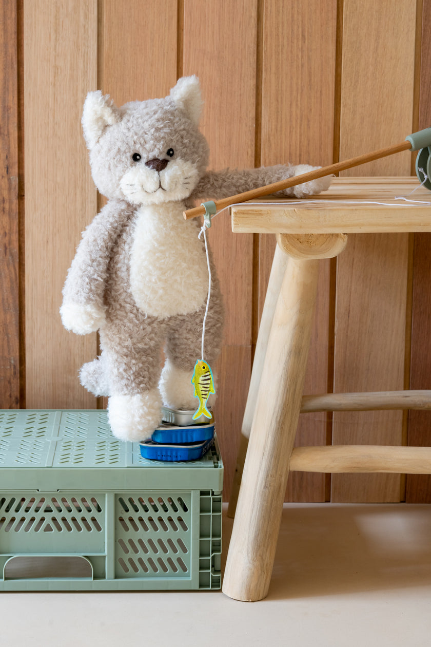 Plush cat toy with a string toy on a green crate next to a wooden stool.