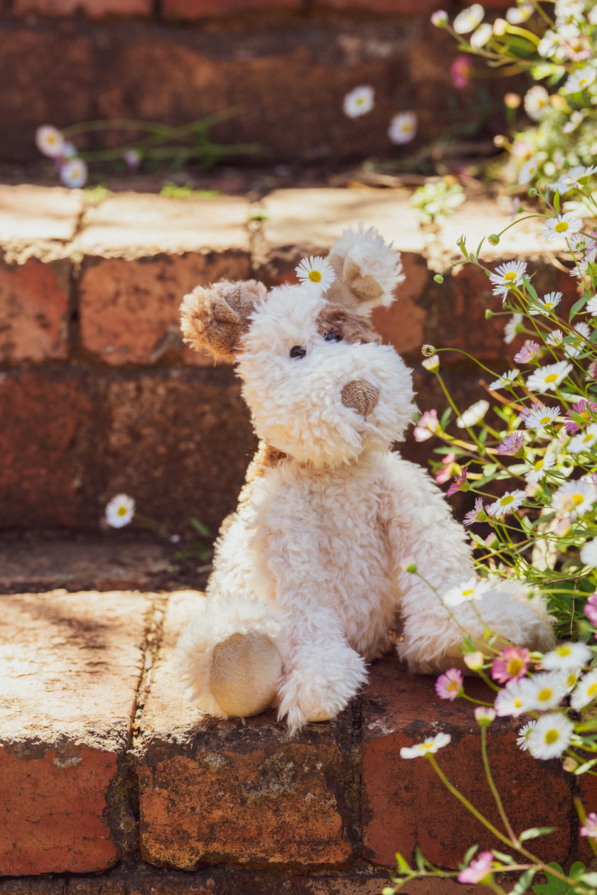 Stuffed dog toy on a brick step with flowers