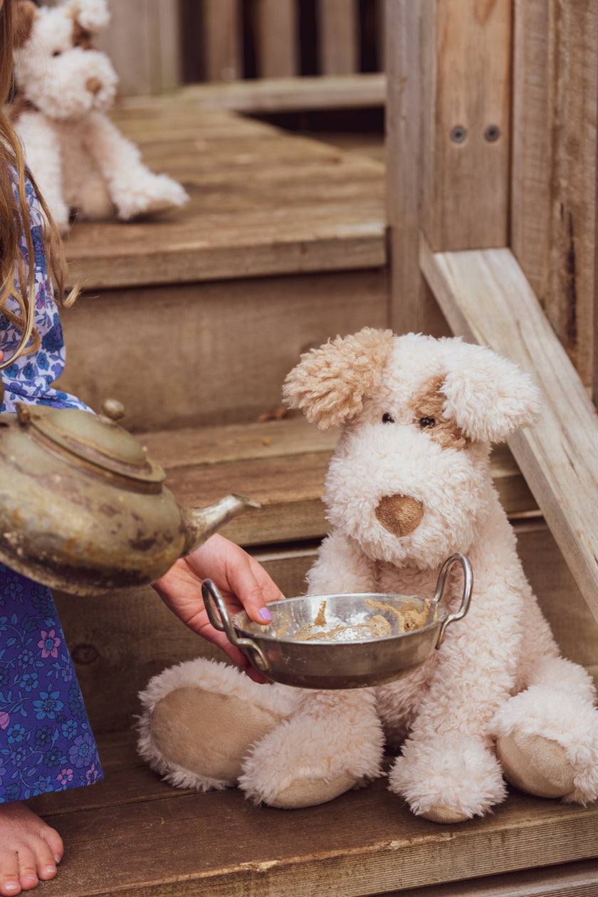 Child holding a teacup next to a stuffed dog on wooden steps