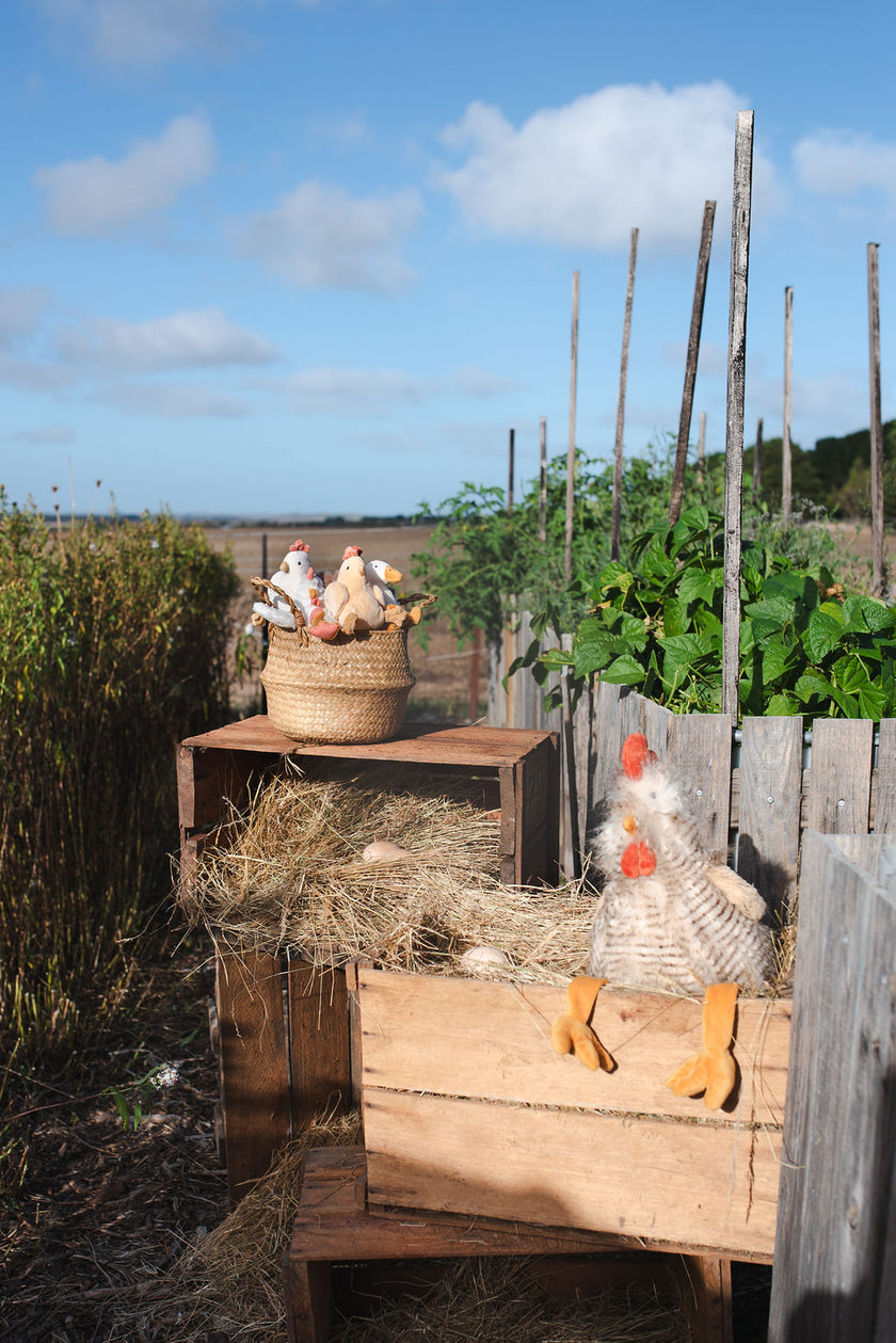 Outdoor scene with a wooden crate, straw, and decorative chicken figure in a garden setting. Soft plush toys farm animals