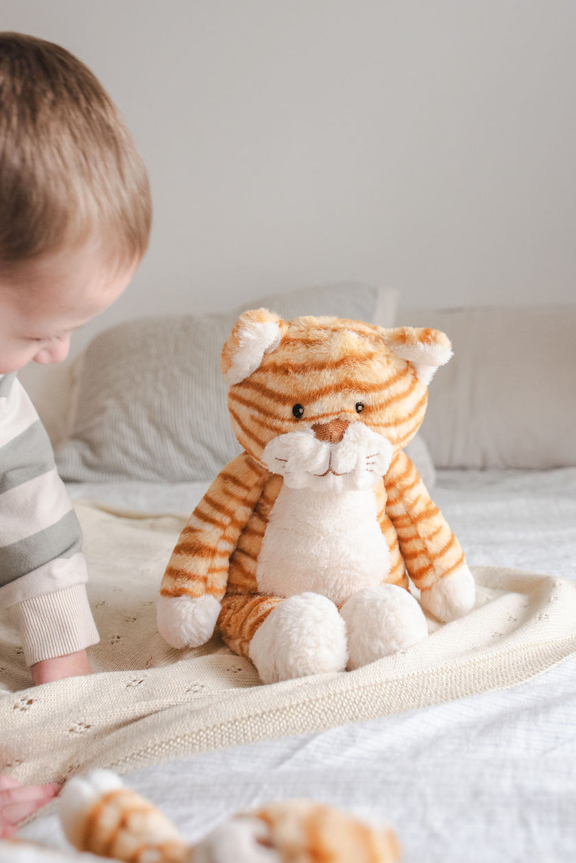 Child playing with a plush tiger toy on a bed