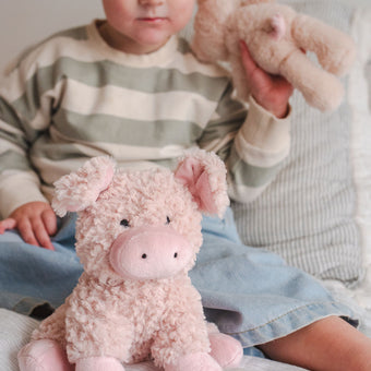 Child holding a plush toy pig and teddy bear on a bed
