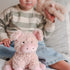 Child holding a plush toy pig and teddy bear on a bed