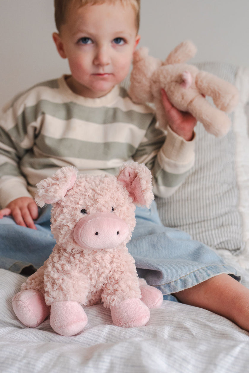 Child holding a plush toy pig and teddy bear on a bed