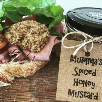 Sandwich with meat and bread, accompanied by a jar of 'Mumma's Spiced Honey Mustard' on a wooden surface.