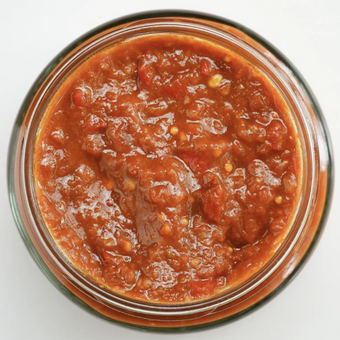 A jar of spicy tomato relish with a rich red color and visible chunky texture.