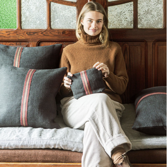 Woman holding a pillow with striped pattern on a wooden bench  Libeco.