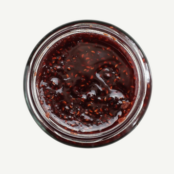 Jar of dark red jam with visible seeds on a white background