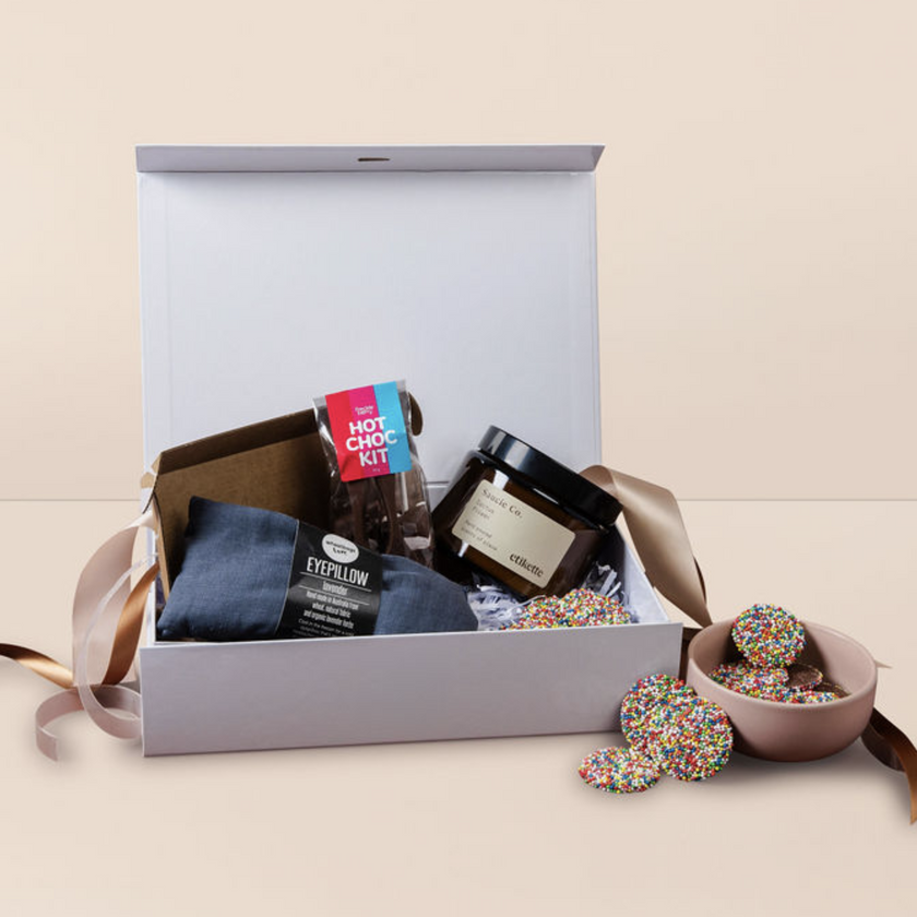 Gift box care hamper with various items including a hot chocolate kit and candies on a beige background