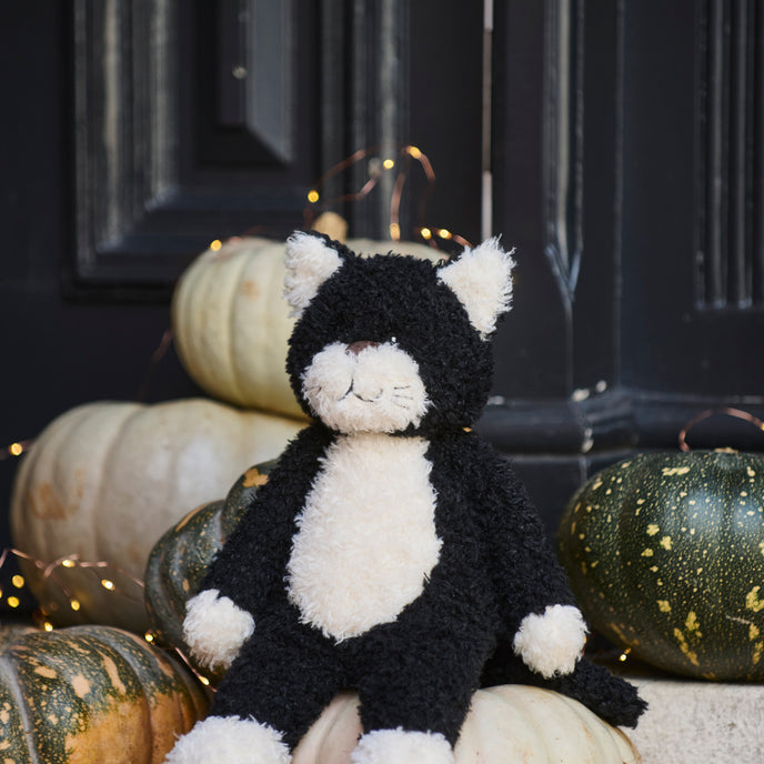 Black and white cat plush toy sitting on pumpkins with a dark background