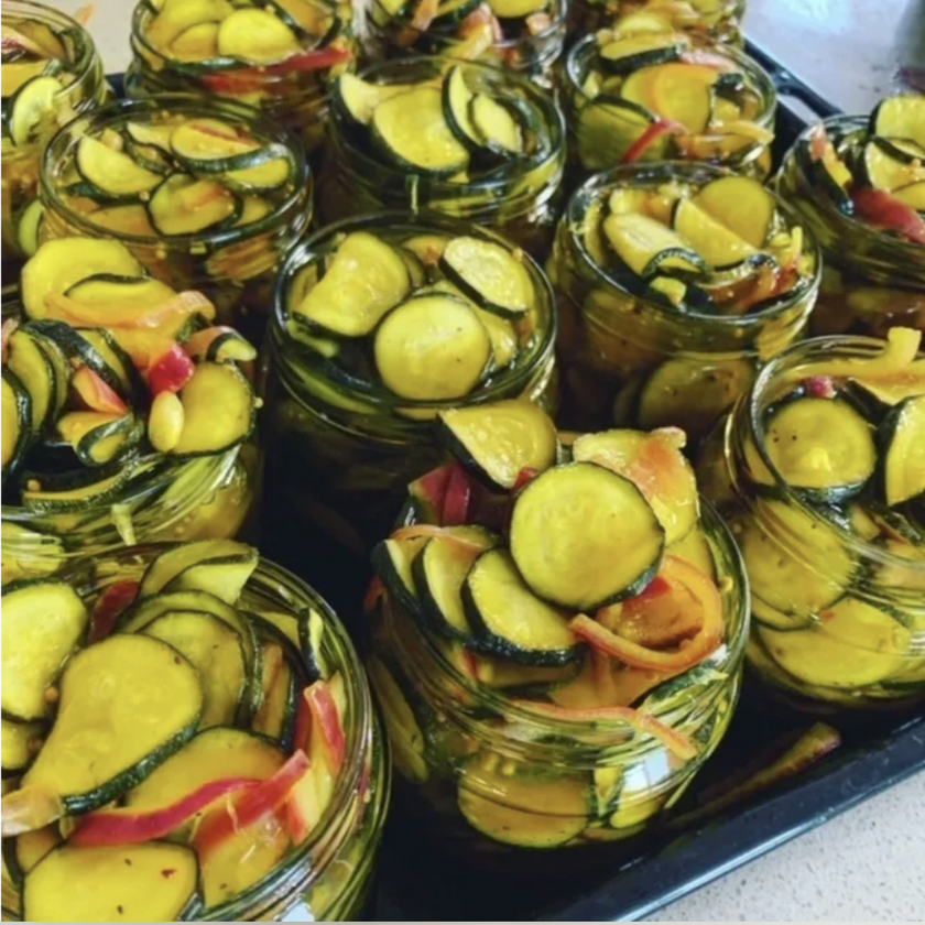 Jars of pickled vegetables including zucchini and bell peppers on a tray.