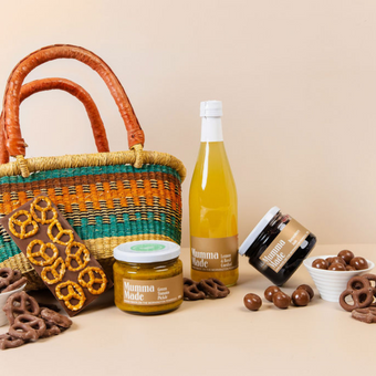 Bottle of lemonade, jar of jam, and basket with snacks on a beige background. Hamper for gifts, corporate, thank you, teachers