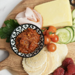 Platter with cheese, crackers, fruits, and a small bowl of spread on a wooden board.