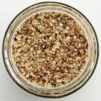 Glass jar filled with a mixture of seeds on a light gray background