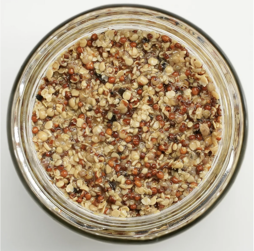 Glass jar filled with a mixture of seeds on a light gray background