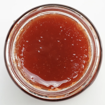 Close-up of a jar with red jelly-like substance on a white background